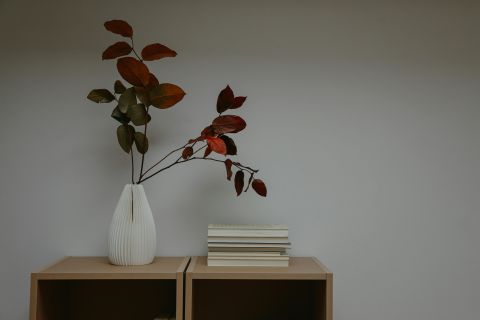 A small ribbed white vase holding autumn leaves on a beech sideboard.